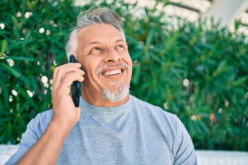 Middle age hispanic grey-haired man smiling happy talking on the smartphone at the park.