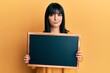 © Krakenimages.com - Young hispanic woman holding blackboard skeptic and nervous, frowning upset because of problem. negative person.