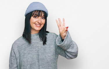 Young hispanic woman wearing cute wool cap showing and pointing up with fingers number three while smiling confident and happy.