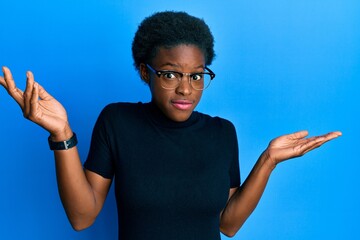 Canvas Print - Young african american girl wearing casual clothes and glasses clueless and confused with open arms, no idea and doubtful face.