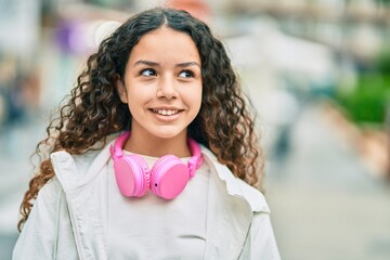 Wall Mural - Hispanic child girl smiling happy using headphones at the city.