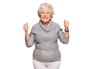 Wall Mural - Senior grey-haired woman wearing casual winter sweater angry and mad raising fists frustrated and furious while shouting with anger. rage and aggressive concept.