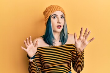 Wall Mural - Young modern girl wearing wool hat afraid and terrified with fear expression stop gesture with hands, shouting in shock. panic concept.