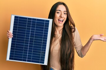 Sticker - Young hispanic girl holding photovoltaic solar panel celebrating achievement with happy smile and winner expression with raised hand