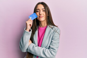 Sticker - Young hispanic girl holding credit card relaxed with serious expression on face. simple and natural looking at the camera.