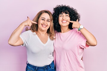 Poster - Middle east mother and daughter wearing casual clothes smiling cheerful showing and pointing with fingers teeth and mouth. dental health concept.