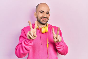 Canvas Print - Young bald man wearing gym clothes and using headphones smiling looking to the camera showing fingers doing victory sign. number two.