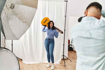 Sticker - Beautiful model holding guitar posing for professional photographer man at photography studio.