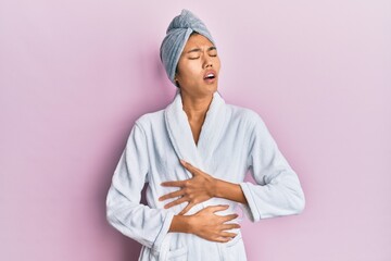 Poster - Young chinese woman wearing shower towel cap and bathrobe with hand on stomach because nausea, painful disease feeling unwell. ache concept.