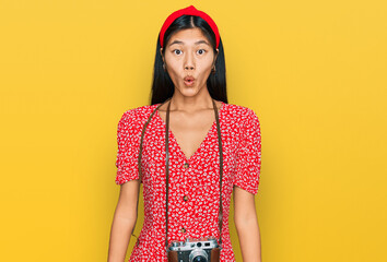 Sticker - Beautiful young asian woman wearing dress and vintage camera scared and amazed with open mouth for surprise, disbelief face