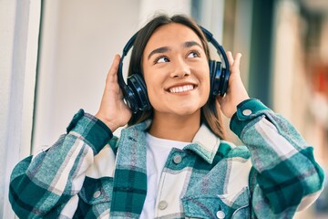 Sticker - Young latin girl smiling happy using headphones at the city.