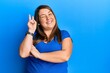 Beautiful brunette plus size woman wearing casual blue t shirt smiling with happy face winking at the camera doing victory sign. number two.