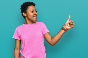 Wall Mural - Young african american woman wearing casual clothes looking proud, smiling doing thumbs up gesture to the side