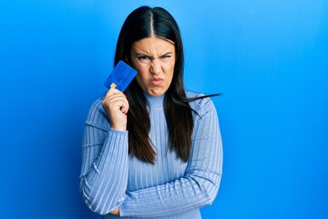 Poster - Beautiful brunette woman holding credit card skeptic and nervous, frowning upset because of problem. negative person.