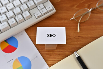 Leinwandbilder - There is a card with the word of SEO which is an abbreviation for Search Engine Optimization on the desk with a laptop, a pen and glasses.
