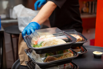 Wall Mural - A view of an employee preparing to pack several food to-go containers, in a restaurant kitchen setting.