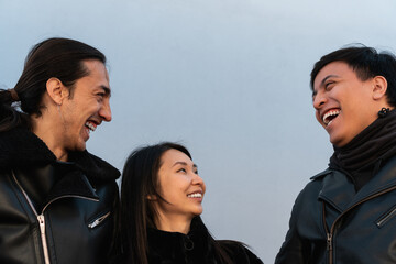 three friends laughing, dressed in black, an Asian American woman and two Latino men