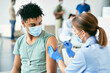 © Drazen - Young black man receiving COVID-19 vaccine during immunization at vaccination center.