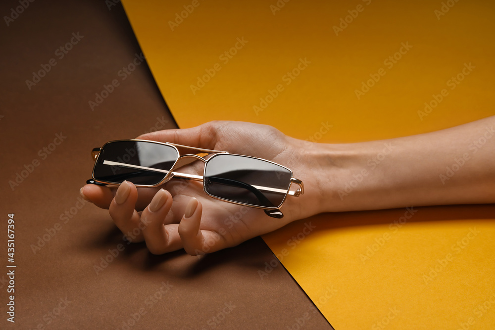 Female hand with stylish sunglasses on colorful background