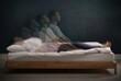 Somnambulist rising from bed near dark wall indoors, multiple exposure. Sleepwalking