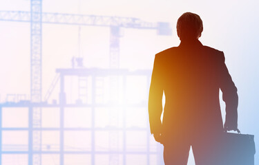 Poster - Construction business. Investment in real estate. Silhouette of a man in a business suit on the background of construction. A businessman on the background of houses under construction and cranes.