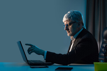 Poster - The man in the business suit raised a finger to the laptop screen. A businessman works with a contract on a PC. A man reads a document. A man with gray hair is working at a computer.