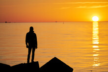 Woman Or Man Standing On Rock Looking Straight. Nature And Beauty Concept. Orange Sundown. Girl Silhouette At Sunset.