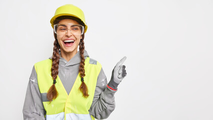 Positive woman builder on construction site demonstrates something over blank space wears hard hat protective glasses uniform has engineering career isolated over white background. Safety apparel