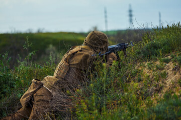 The soldier lies on the ground and aims at the rifle scope