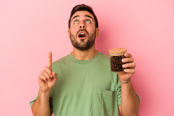 Wall Mural - Young caucasian man holding a coffee bottle isolated on pink background pointing upside with opened mouth.