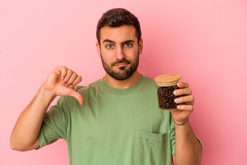 Wall Mural - Young caucasian man holding a coffee bottle isolated on pink background showing a dislike gesture, thumbs down. Disagreement concept.