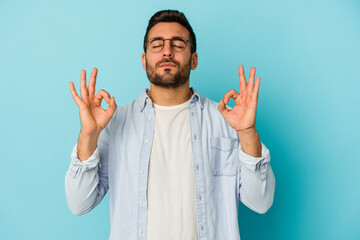 Young caucasian man isolated on blue background relaxes after hard working day, she is performing yoga.