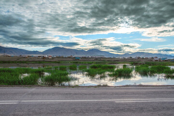 Wall Mural - Mountain landscape in the early morning. The sky is reflected in the lake. In the distance there is a village. The sky is covered with gray clouds. Altai, Kosh-Agach 