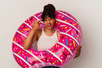 Wall Mural - Young mixed race woman holding an inflatable air donut isolated on white background showing a disappointment gesture with forefinger.