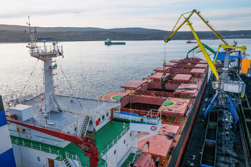 Industrial ships at the mooring wall in the seaport in the Kola Bay.
  The holds of the ship are filled with bulk cargo of mineral origin