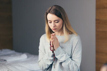 Young woman prays to God, folded her arms on her chest uses a rosary and a crucifix, asks for a better fate