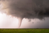 Fototapeta  - A tornado spawns from a thunderstorm in a rural setting during the day. There funnel is very visible with a green meadow full of grass in the foreground.