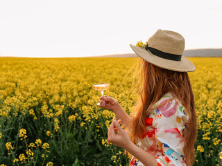 A woman drinking wine in a flowering field at sunset.