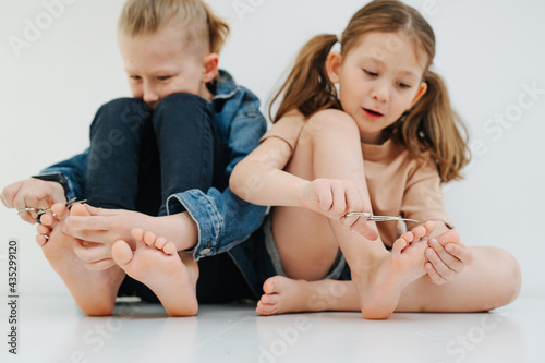 Funny kids. Little siblings with bare feet clipping nails on their toes. Both very focused. Girl is enjoying it, boy is dreading it.