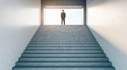 Looking to future concept with businessman on top of stairway between light walls and looking on successful life.