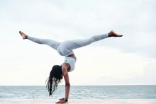 Side View Of Athletic Young Woman Practicing Yoga, Doing Handstand With Splits Pose On Beach
