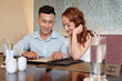 © DragonImages - Smiling young boyfriend and girlfriend sitting at restaurant table and reading menu before ordering food