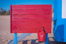 Red Wooden Wall On The Beach With A Red Fire Extinguishing Bucket