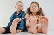 Cute kids with bare feet. Boy is holding scissors in toes, reaching girl's toes
