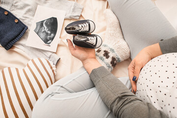 Sticker - Pregnant woman with sonogram image, baby booties and clothes on bed, closeup