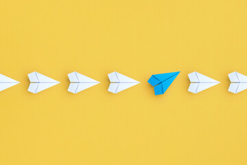 Wall Mural - Business concept for new ideas creativity and innovative solution, Group of white paper plane in one direction and one blue paper plane pointing in different way on yellow background