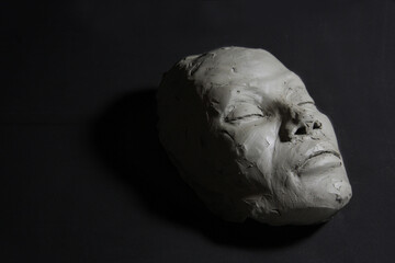 Clay sculpture, with closed eyes. face with shadows, lying on black floor