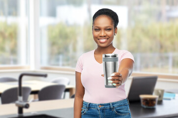 Wall Mural - sustainability and people concept - portrait of african american woman in turquoise shirt with thermo cup or tumbler for hot drinks over home kitchen background