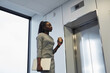 Minimal portrait of African-American businesswoman waiting for elevator in office building and holding coffee cup, copy space