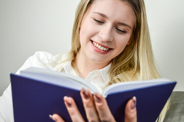 Portrait of a beautiful young blond woman smiling while reading a book